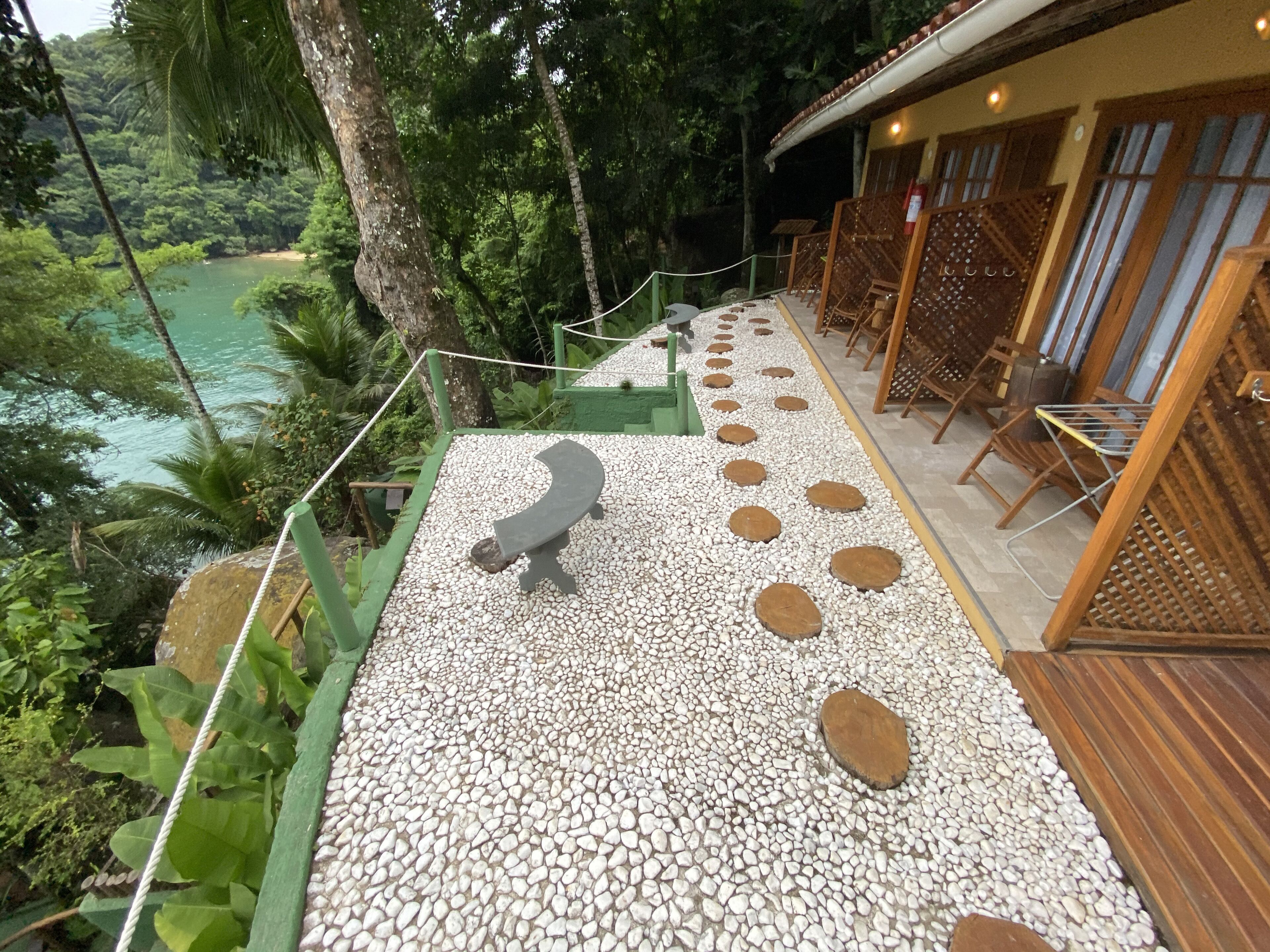 Una terrazza con un vialetto in pietra, sedie a sdraio in legno e vista su una rigogliosa foresta e un corpo d'acqua.