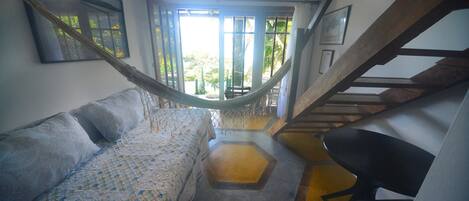 A room with a hammock, a bed, a chair, and a staircase leading to an outdoor area.