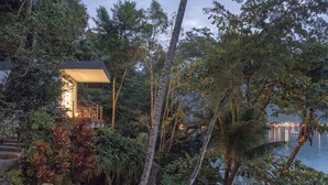 A secluded house with a staircase leading to a deck, surrounded by dense tropical vegetation and overlooking a calm body of water. - Asalem (Angra dos Reis)