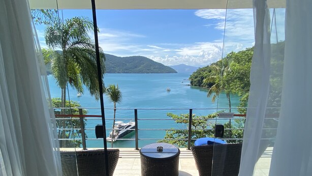 A balcony with wicker furniture, a view of a calm sea, and a mountainous landscape. - Asalem (Angra dos Reis)