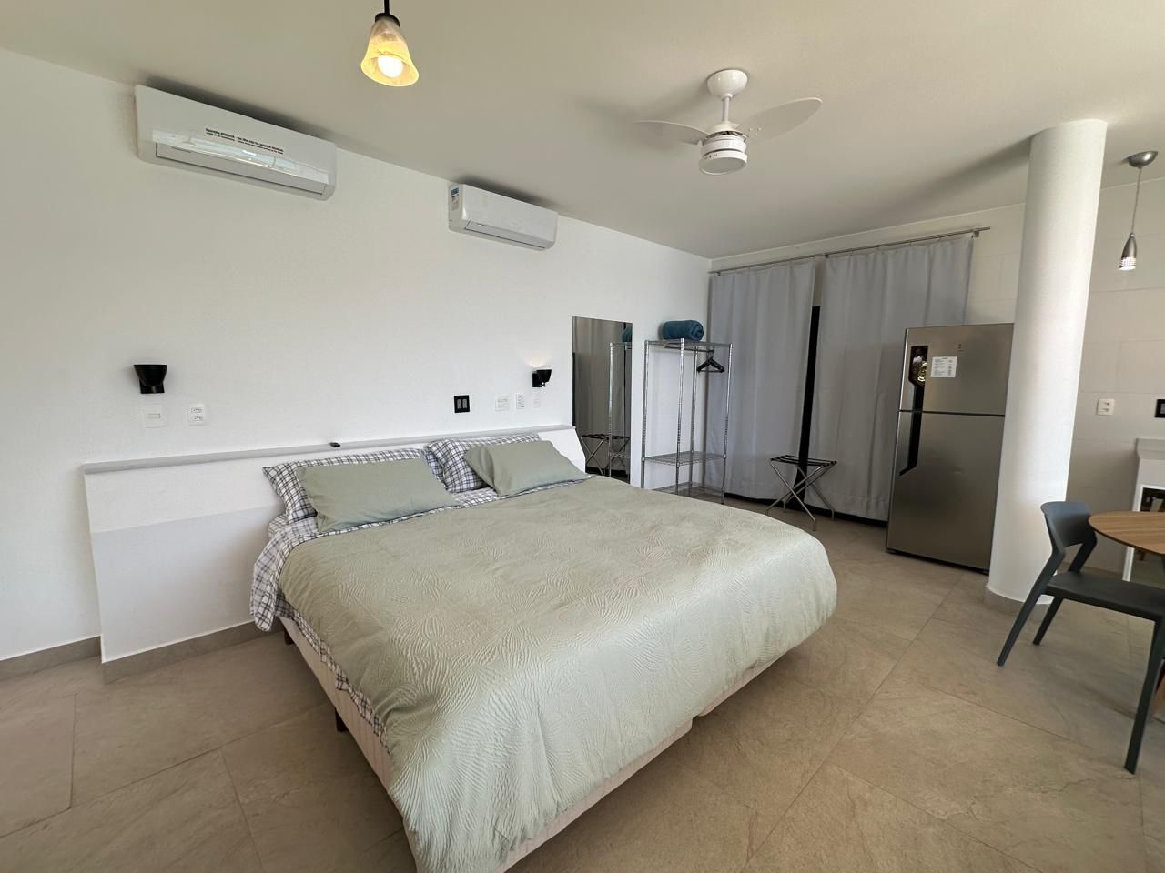 Un dormitorio moderno con una cama grande, una mesita, un refrigerador y un ventilador de techo.