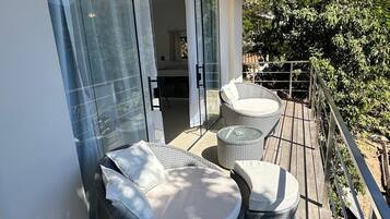 Una terraza con mobiliario de mimbre y un ventanal corredera que da a un espacio interior.