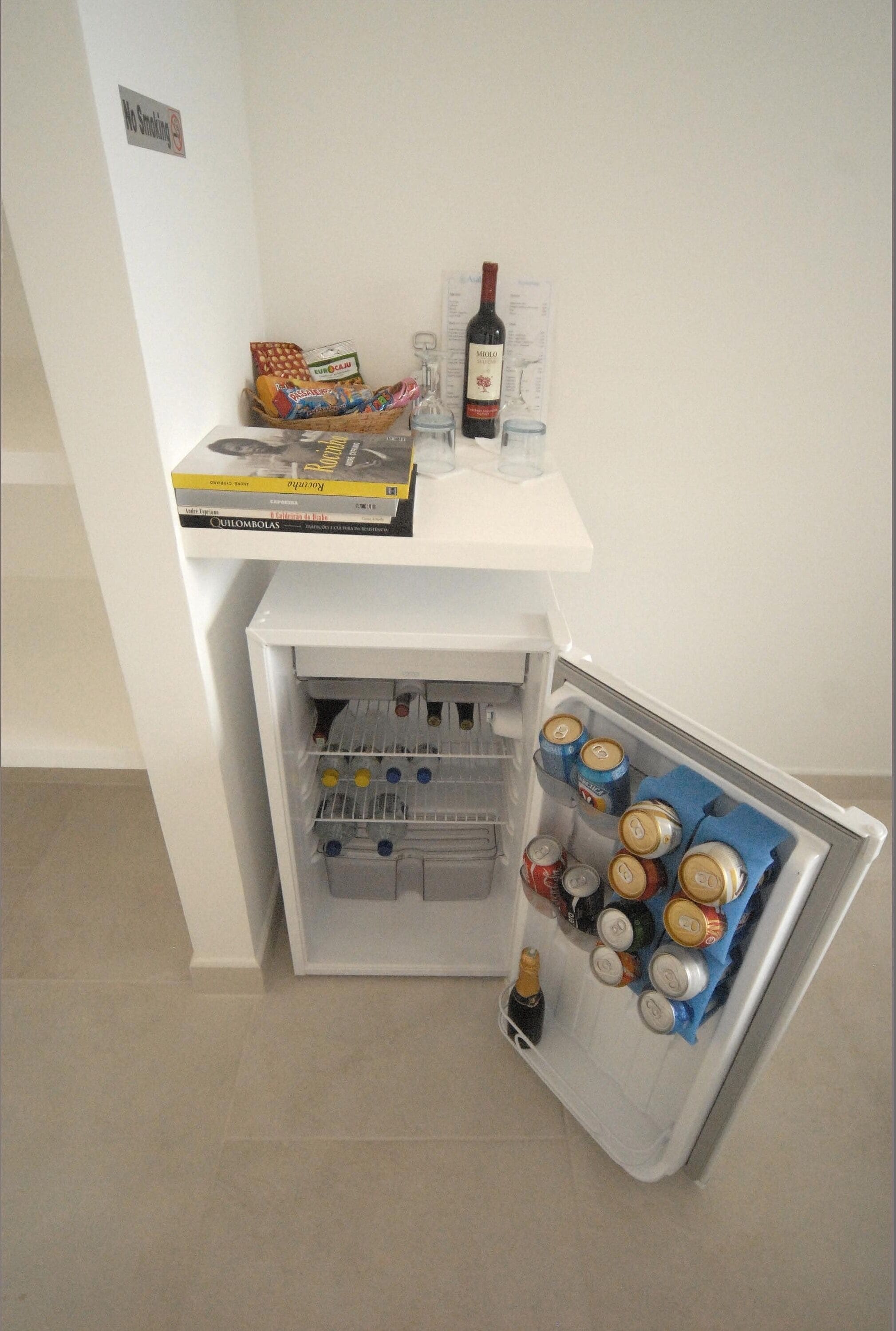 A small refrigerator with a wine bottle, cans, and a box of snacks.