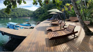 A wooden deck with lounge chairs and umbrellas overlooking a calm lake with boats. - Asalem (Angra dos Reis)