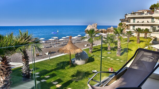 A balcony with a view of the sea, palm trees, and a thatched umbrella. - Hotel Sporting Club (Altavilla Milicia)