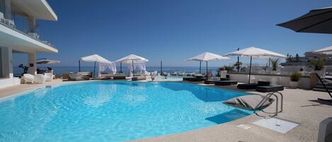 A swimming pool with lounge chairs and umbrellas, overlooking a clear blue sky and sea.