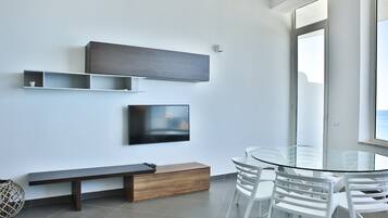 Una habitación moderna con una mesa de vidrio, sillas blancas, un banco de madera, un televisor de pantalla plana y estantes empotrados.