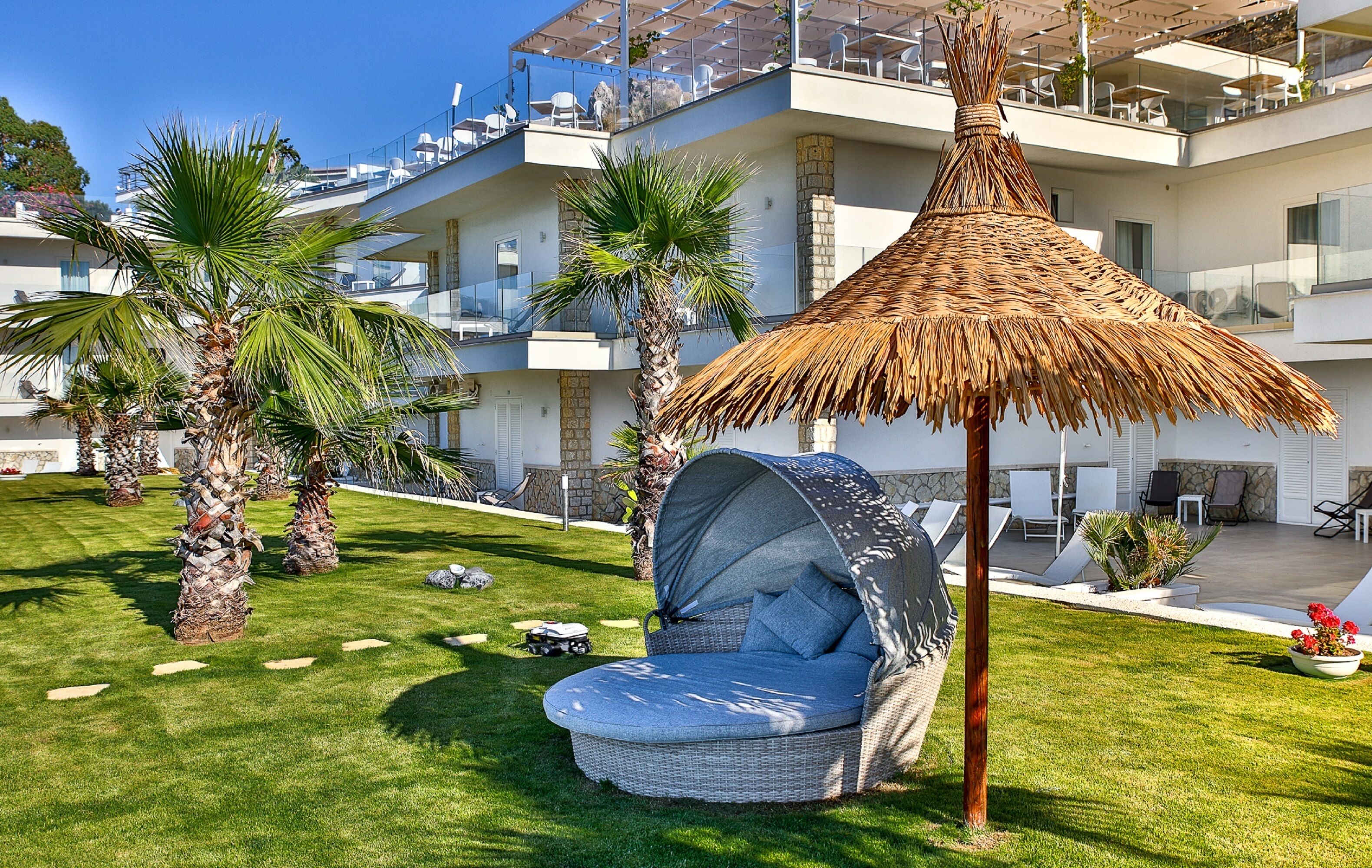 A modern hotel with a rooftop terrace, outdoor seating area, and palm trees.
