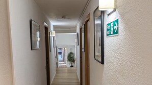Pasillo de hotel con suelo de madera, paredes blancas, cuadros enmarcados y señal de salida de incendios.