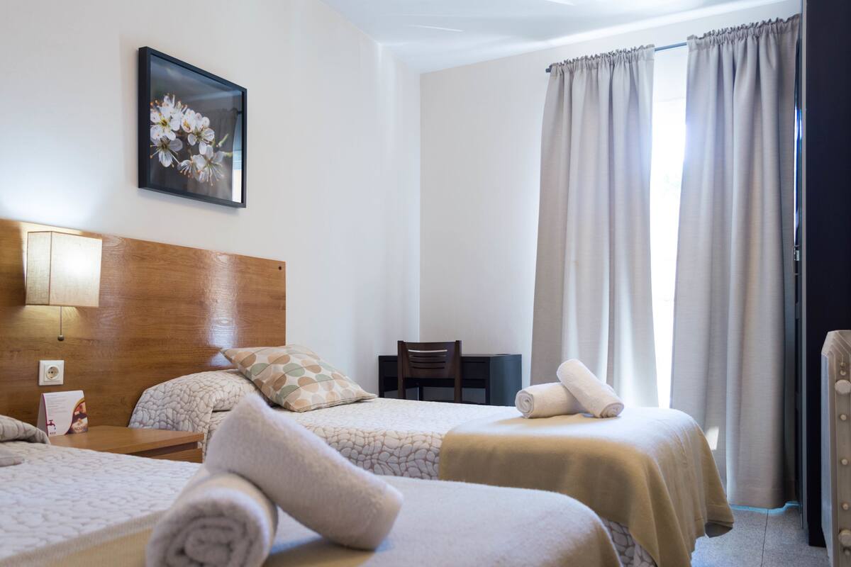 A hotel room with two beds, a desk, a chair, a lamp, and a painting on the wall.