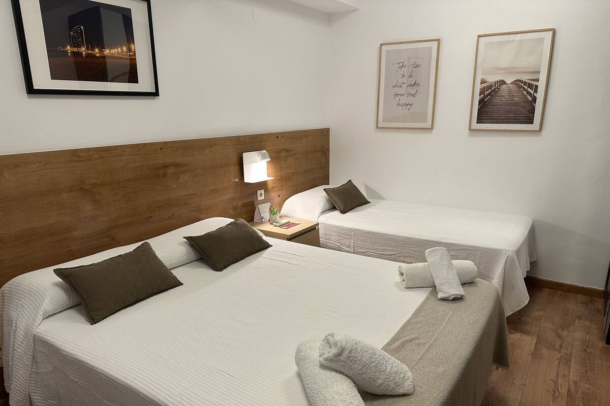A hotel room with two beds, a wooden headboard, a nightstand with a lamp, and two framed pictures on the wall.