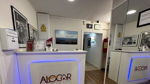 Un mostrador de recepción con retroiluminación azul, marcos con certificados y un cuadro de un paisaje urbano en la parte superior.
