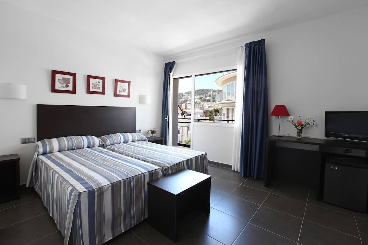 Habitación de hotel con cama, escritorio, televisor y balcón con vista a edificios.