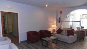 A lobby with a sofa, two armchairs, a coffee table, and a lamp. There is a fire extinguisher on the wall and a door with frosted glass panels. - Hotel Marblau Tossa (Tossa de Mar)