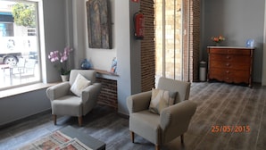 A room with two checkered armchairs, a small table, a vase with flowers, a fireplace, and a brick wall. - Hotel Marblau Tossa (Tossa de Mar)