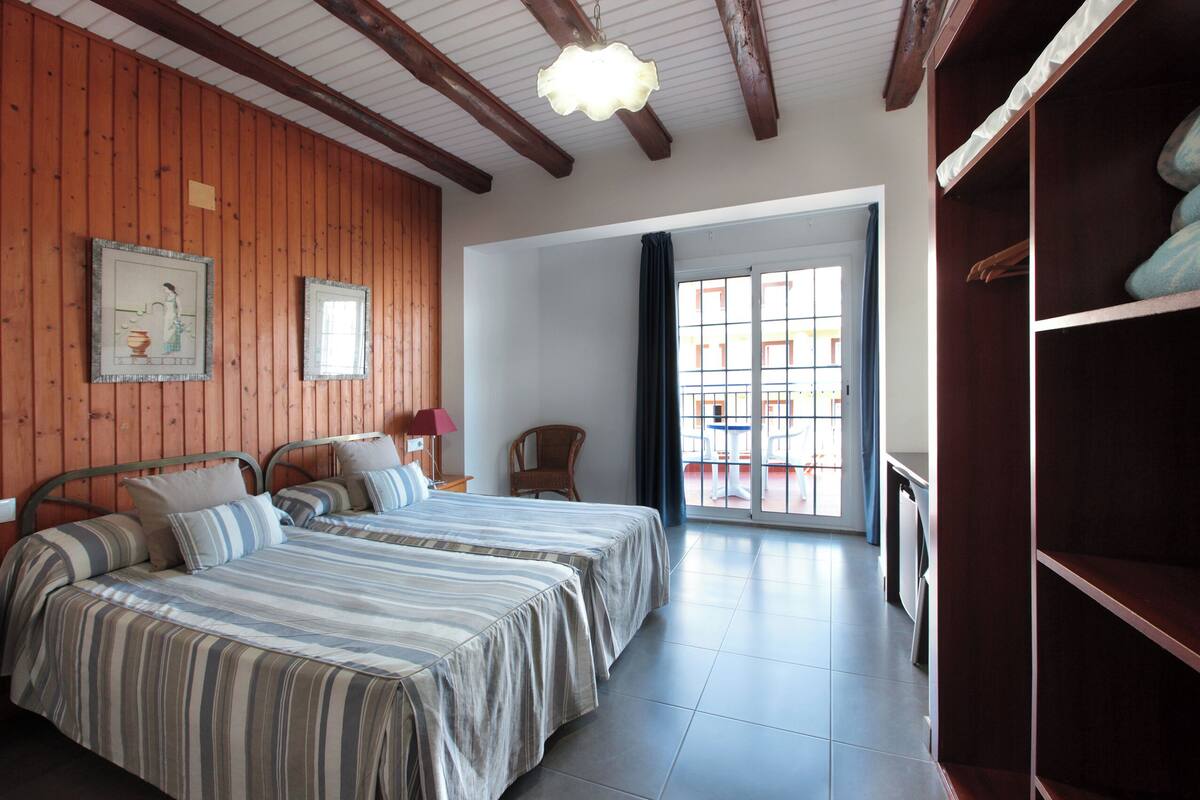 Una habitación con dos camas, paredes de madera, un ventanal grande y un balcón.