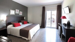 A hotel room with a bed, a desk, a chair, a TV, and a balcony with curtains. - Hotel Marblau Tossa (Tossa de Mar)