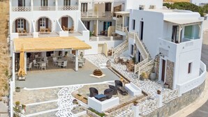 A white building with multiple balconies, outdoor seating, and a staircase leading to the upper floors. - Castillio Hotel (Astypalaia)