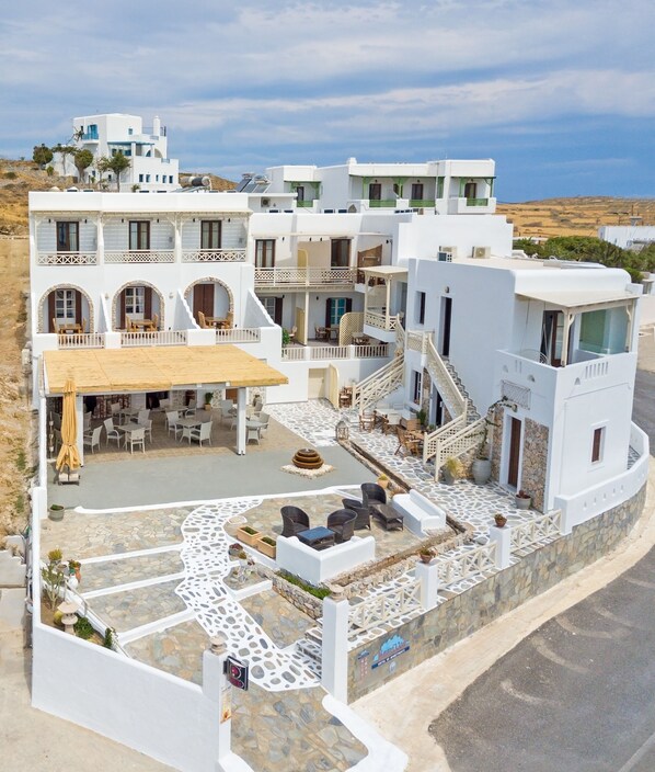 A white building with multiple balconies, outdoor seating, and a staircase leading to the upper floors. - Castillio Hotel (Astypalaia)