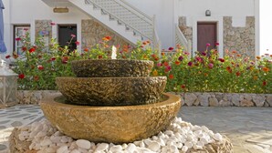 A stone fountain with water cascading into a basin, surrounded by colorful flowers and a stone wall. - Castillio Hotel (Astypalaia)