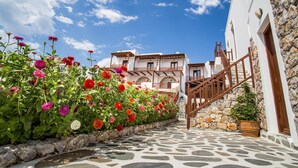 A stone-paved pathway leading to a white building with a wooden staircase and a balcony. - Castillio Hotel (Astypalaia)