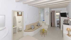A modern, white-themed living room with a sofa, a small table, and a TV. - Castillio Hotel (Astypalaia)