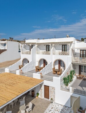 A white building with multiple balconies, outdoor seating, and stone accents. - Castillio Hotel (Astypalaia)