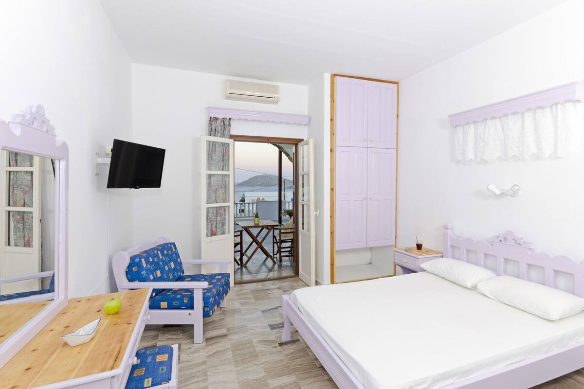 A bedroom with a bed, a desk, a chair, a TV, and a view of the outside.