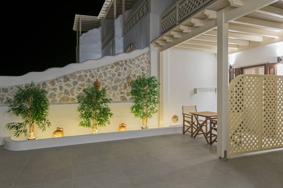 A modern outdoor patio with stone walls, potted plants, and a wooden table and chairs.