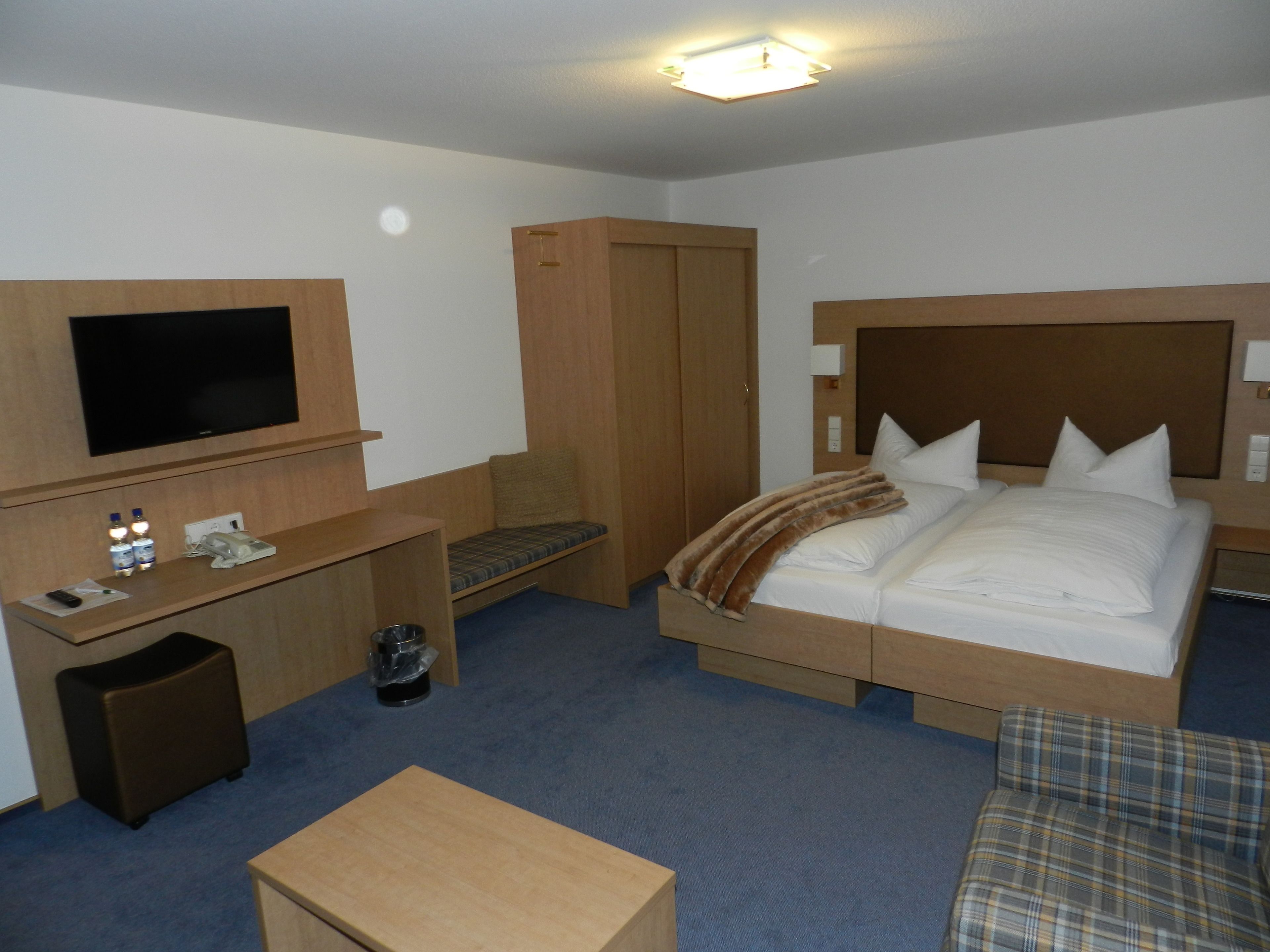 A hotel room with a bed, a desk, a television, a wardrobe, and a small table.