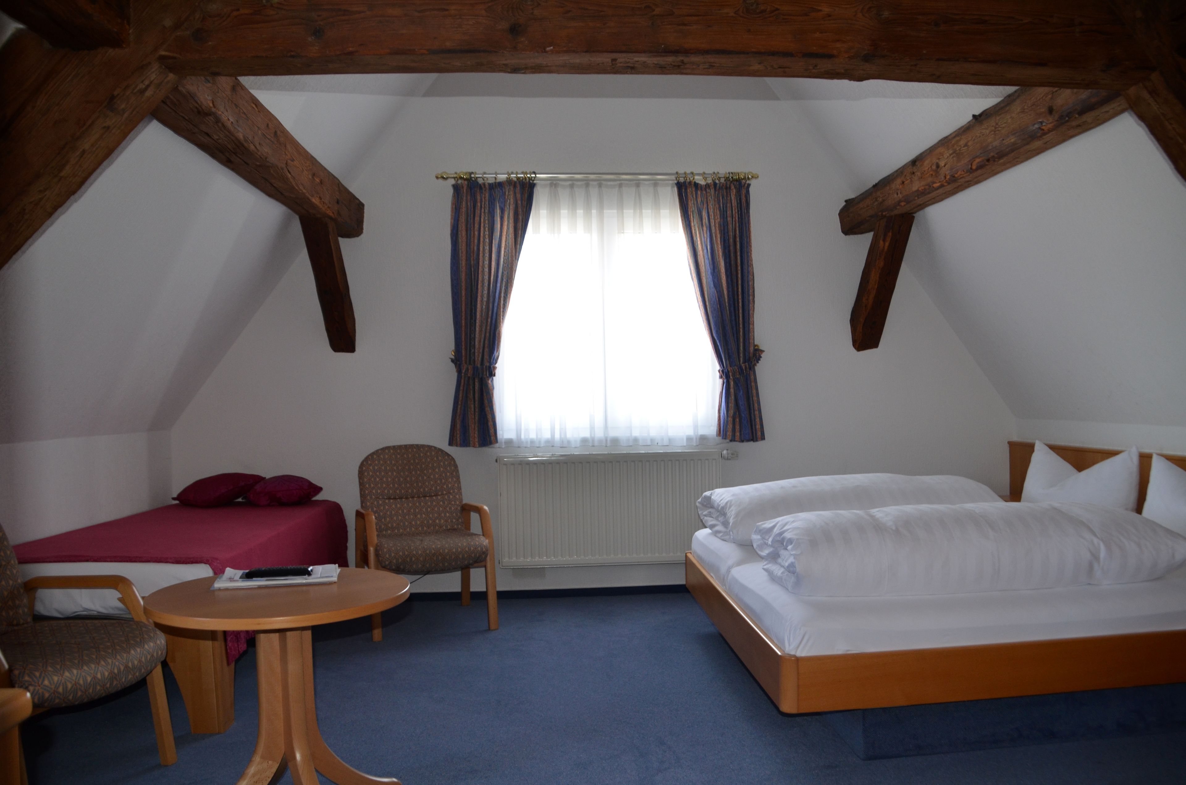 Une chambre à coucher avec un lit, une chaise, une petite table et une fenêtre avec des rideaux.
