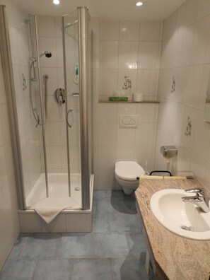 Un baño moderno con cabina de ducha de vidrio, inodoro y lavamanos con encimera de mármol.
