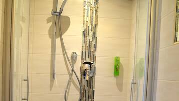 Ducha con puerta de vidrio, pared azulejada y lavamanos blanco con espejo.