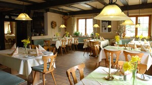 Un restaurant avec des tables et des chaises en bois, des nappes blanches et des lampes suspendues.