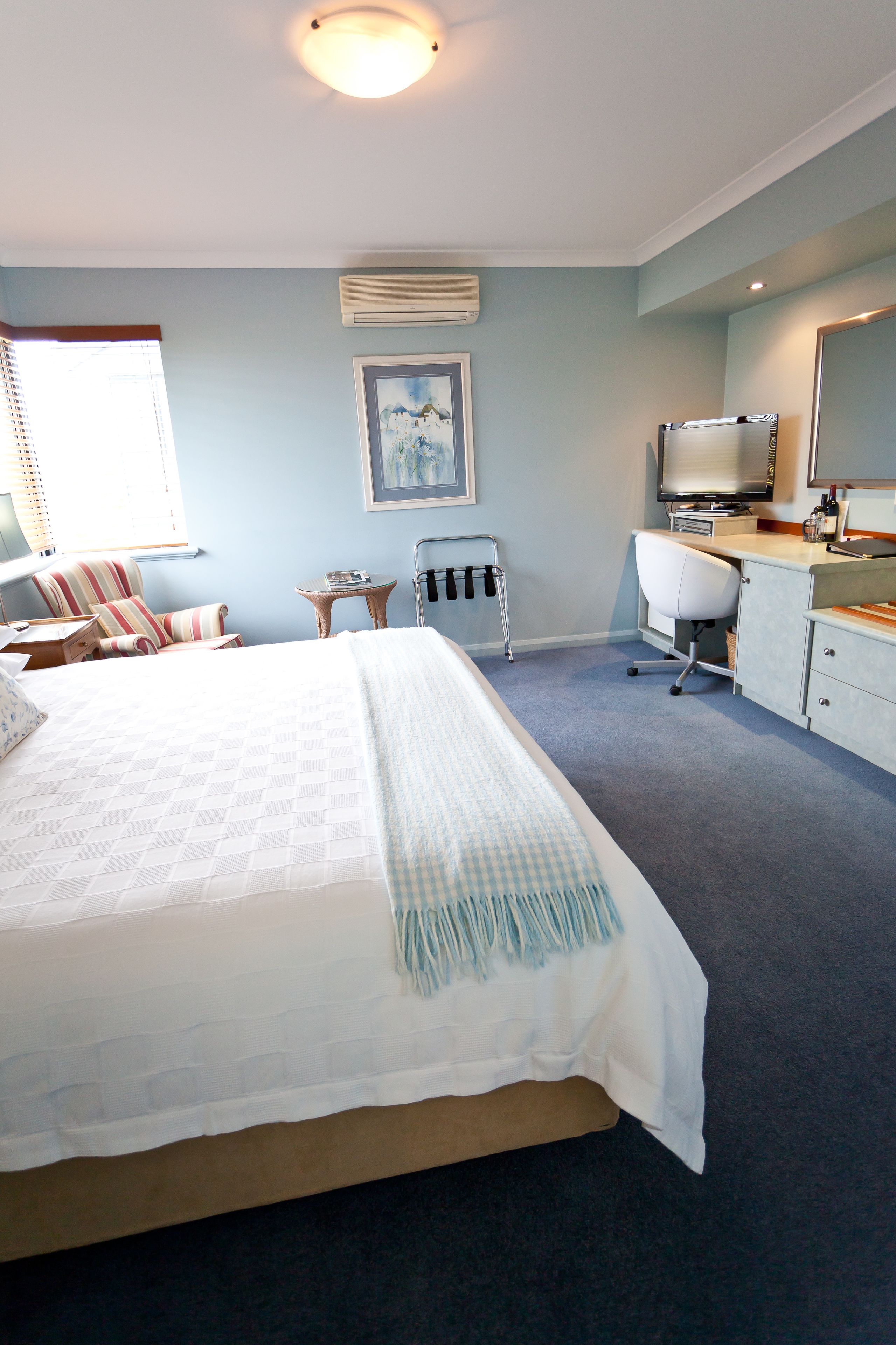 A bedroom with a large bed, a desk, a chair, a TV, and an air conditioning unit.
