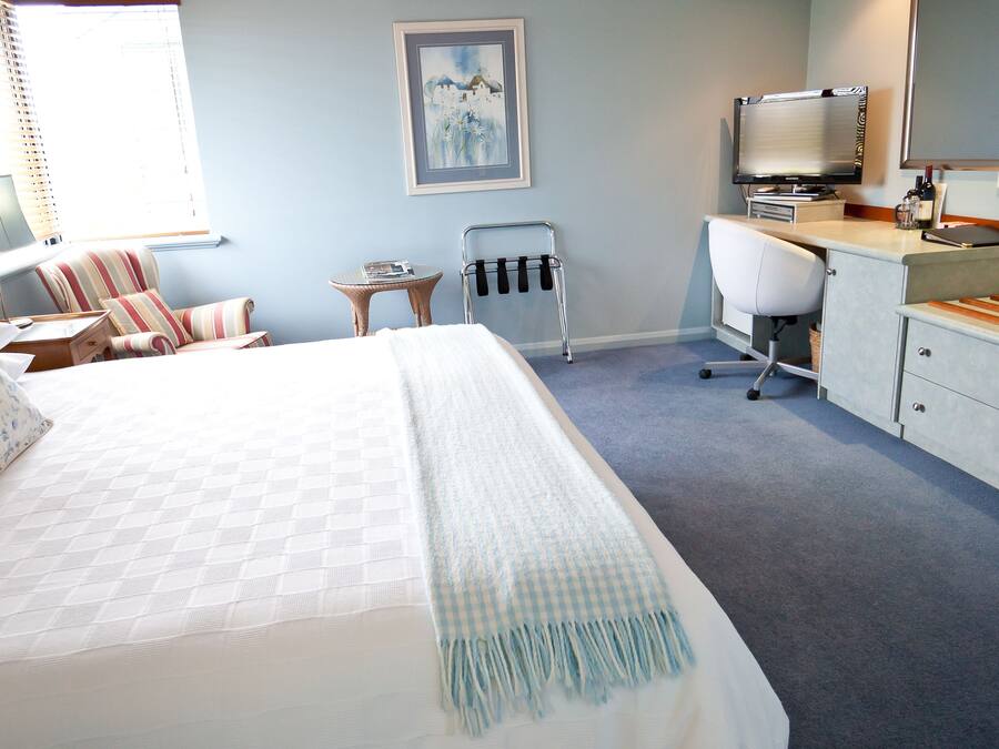 A bedroom with a large bed, a desk, a chair, a TV, and an air conditioning unit.