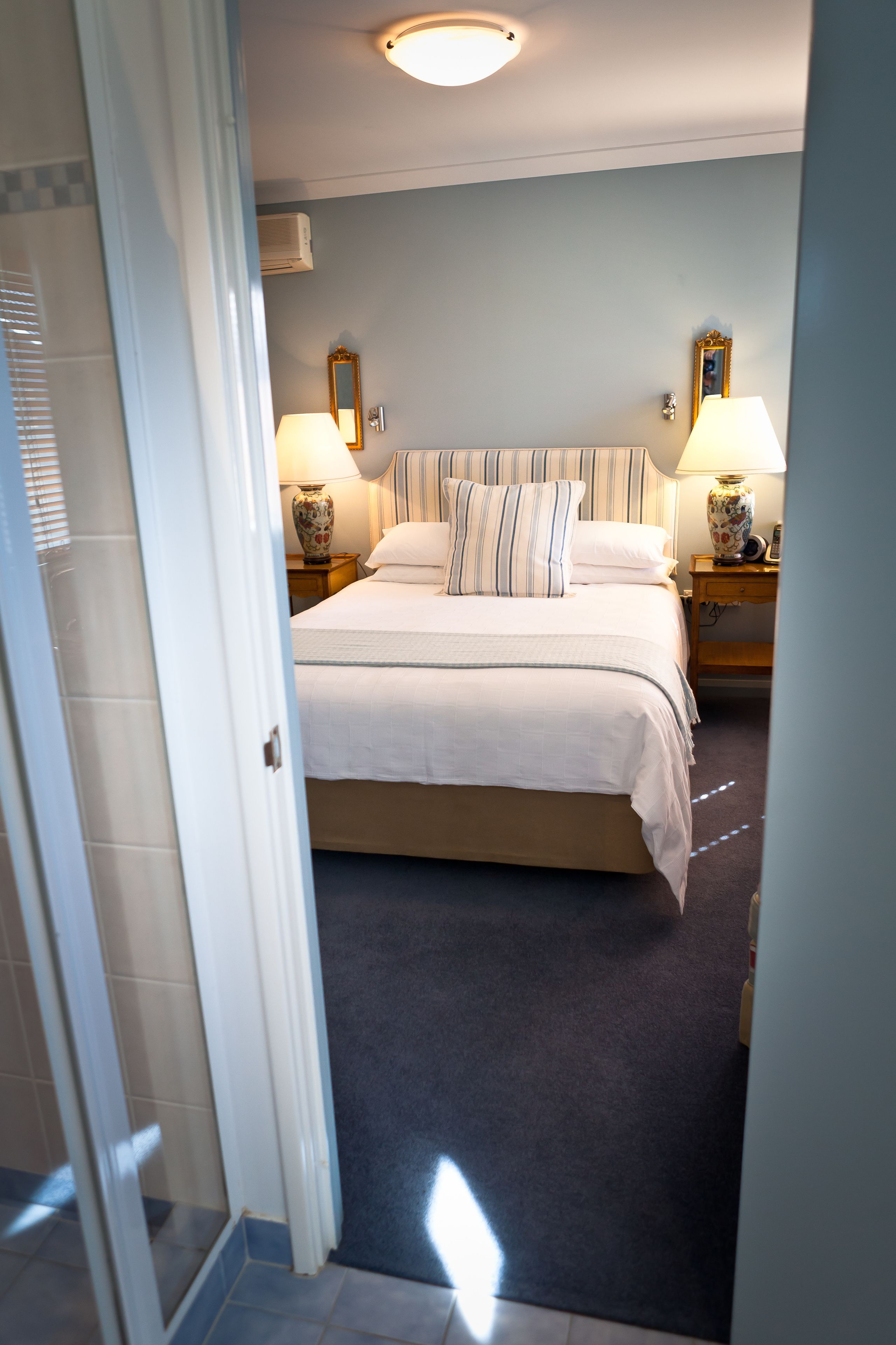 A hotel room with a large bed, two bedside tables with lamps, a mirror, and a carpeted floor.
