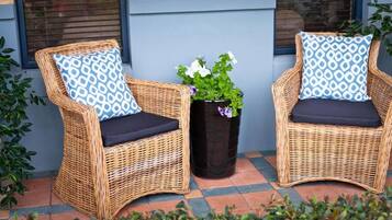 Two wicker chairs with patterned cushions, a potted plant with white flowers, and a tiled floor.