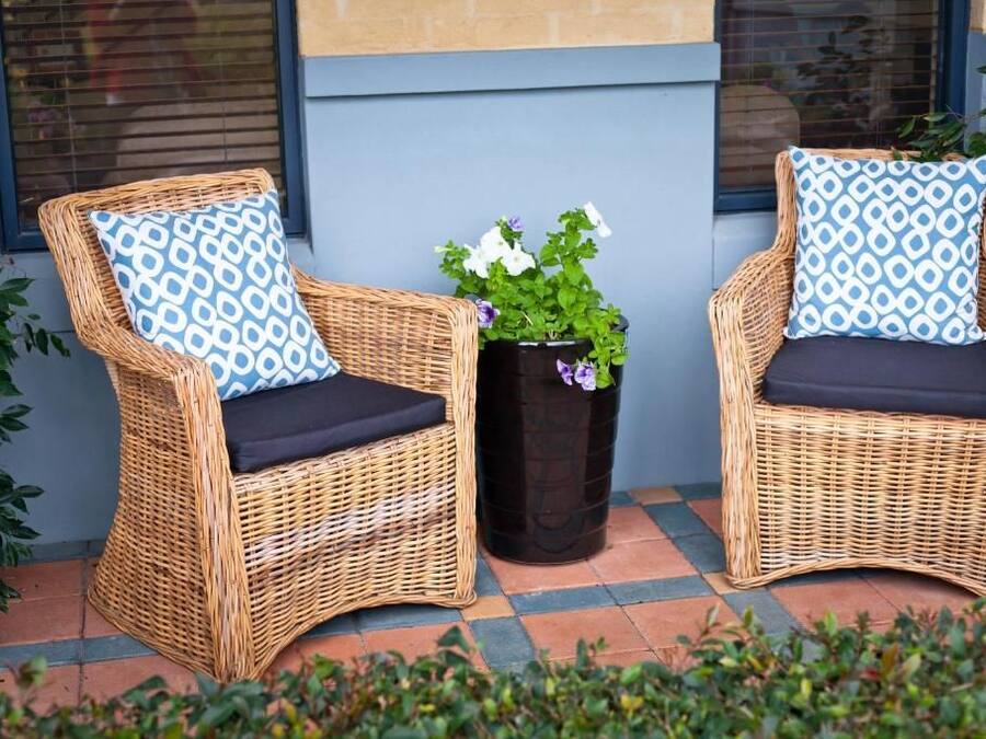 Two wicker chairs with patterned cushions, a potted plant with white flowers, and a tiled floor.