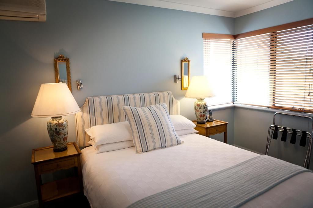 A neatly made bed with striped bedding, two bedside lamps, a mirror, and a radiator.
