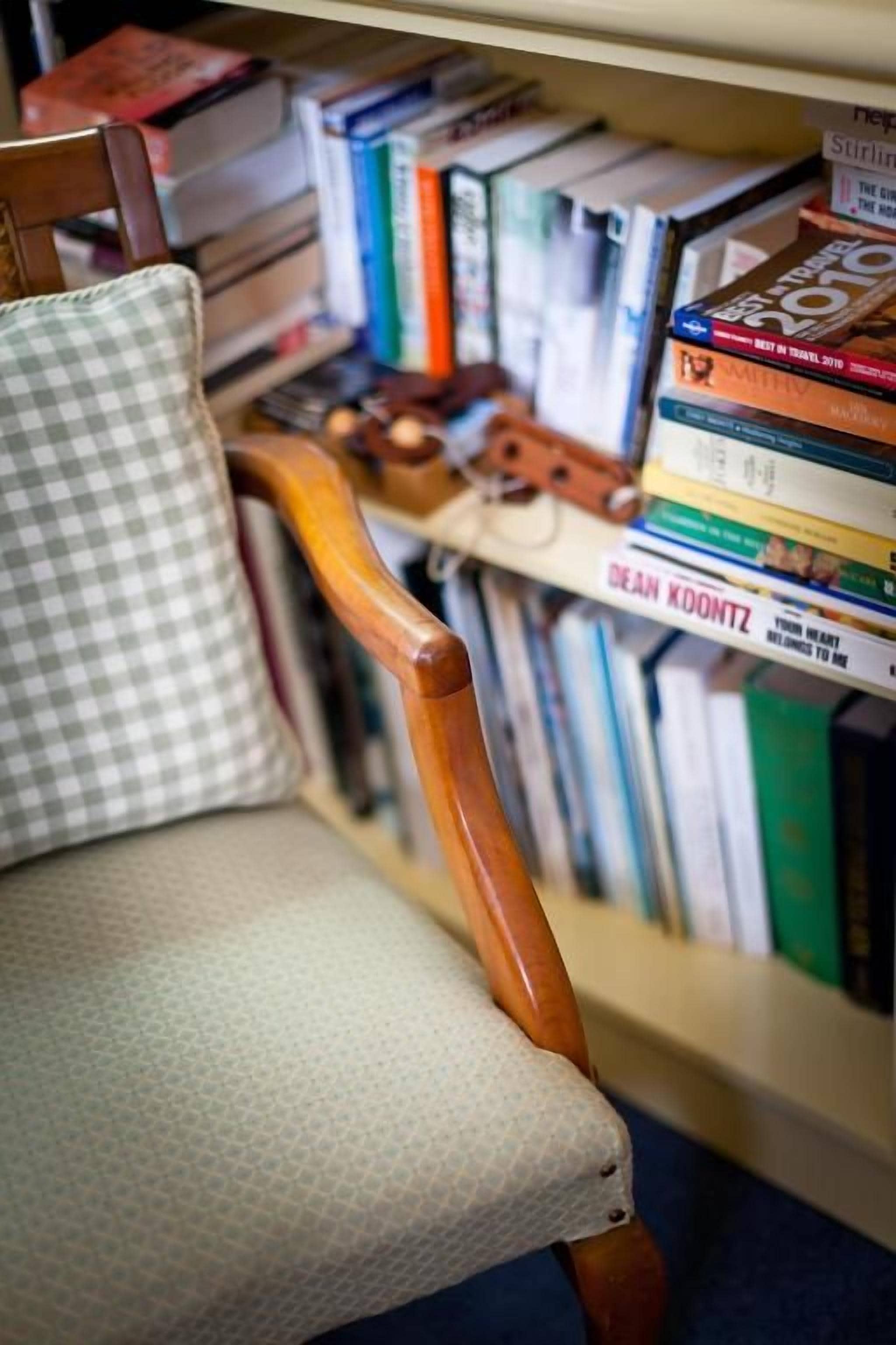 A chair with a checkered cushion and a wooden armrest, positioned in front of a bookshelf filled with books.