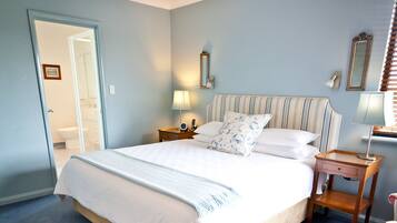 A neatly made bed with white linens and a striped headboard, a bedside table with a lamp, and a mirror on the wall.