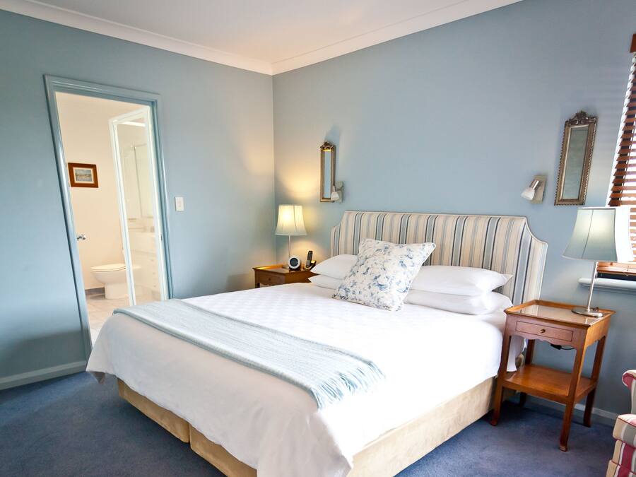 A neatly made bed with white linens and a striped headboard, a bedside table with a lamp, and a mirror on the wall.