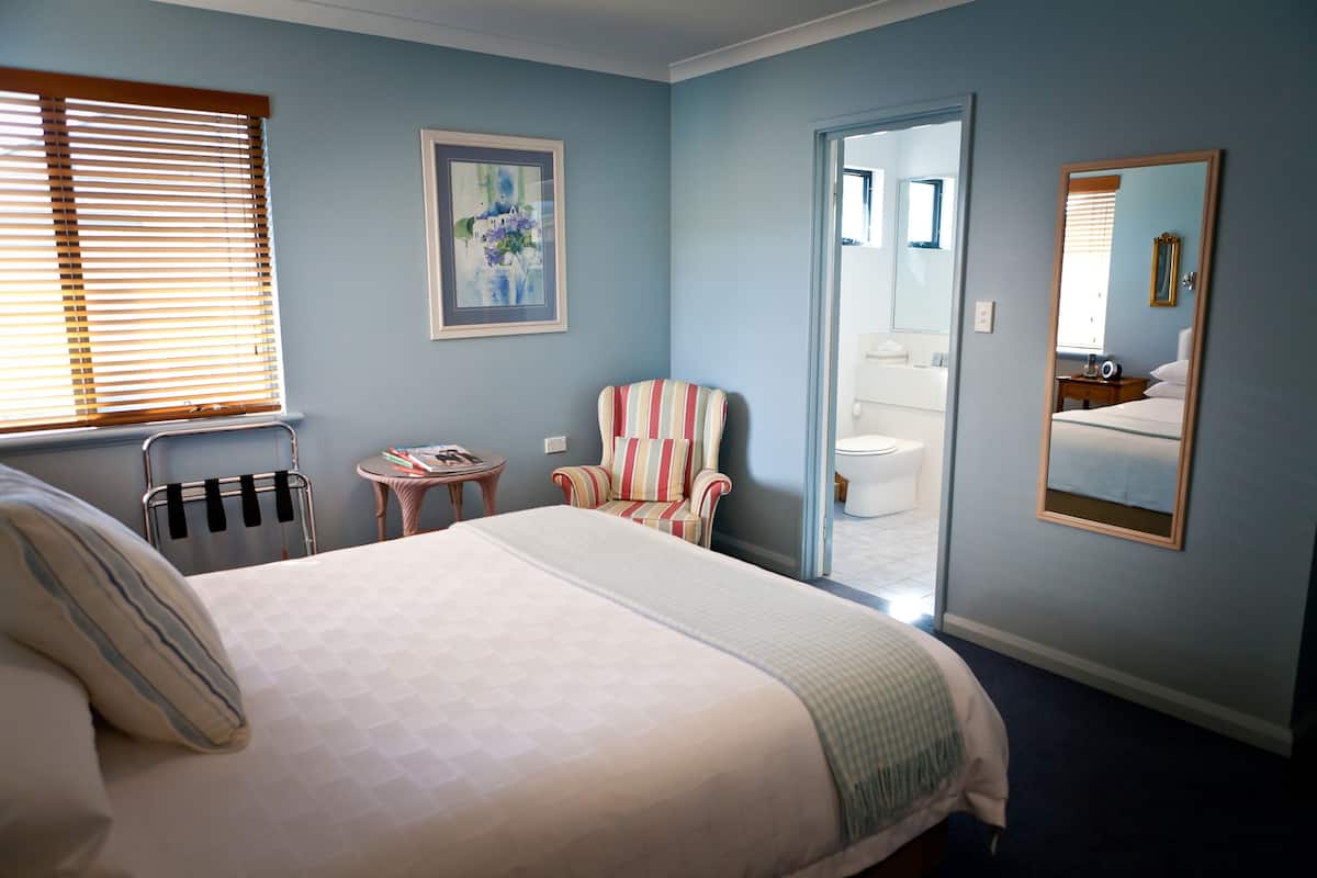 A bedroom with a bed, a striped armchair, a small table, and a mirror.