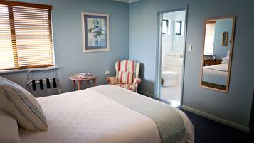 A bedroom with a bed, a striped armchair, a small table, and a mirror.
