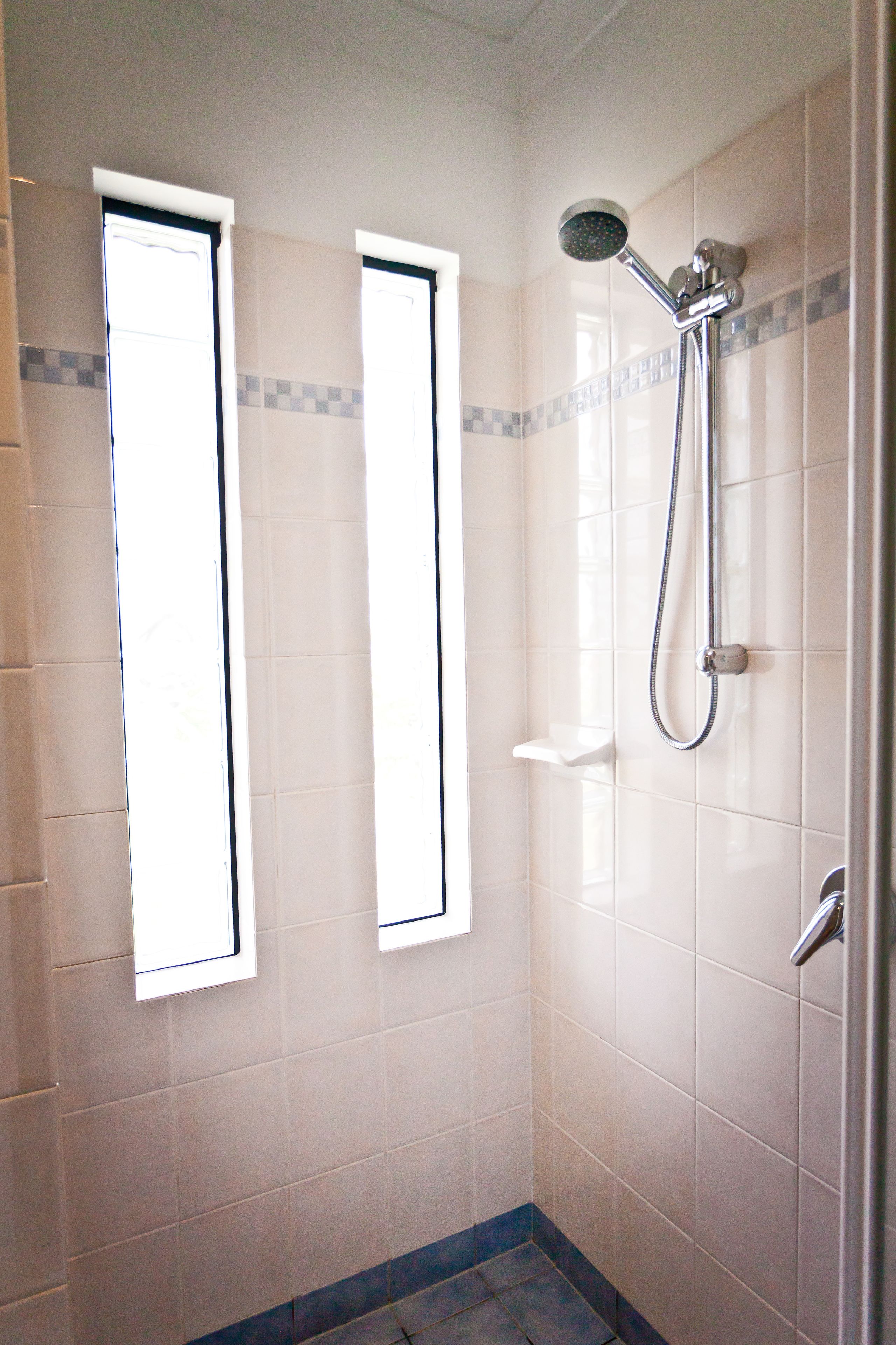 Un pequeño espacio de ducha con azulejos, un cabezal de ducha manual y un grifo instalado en la pared.