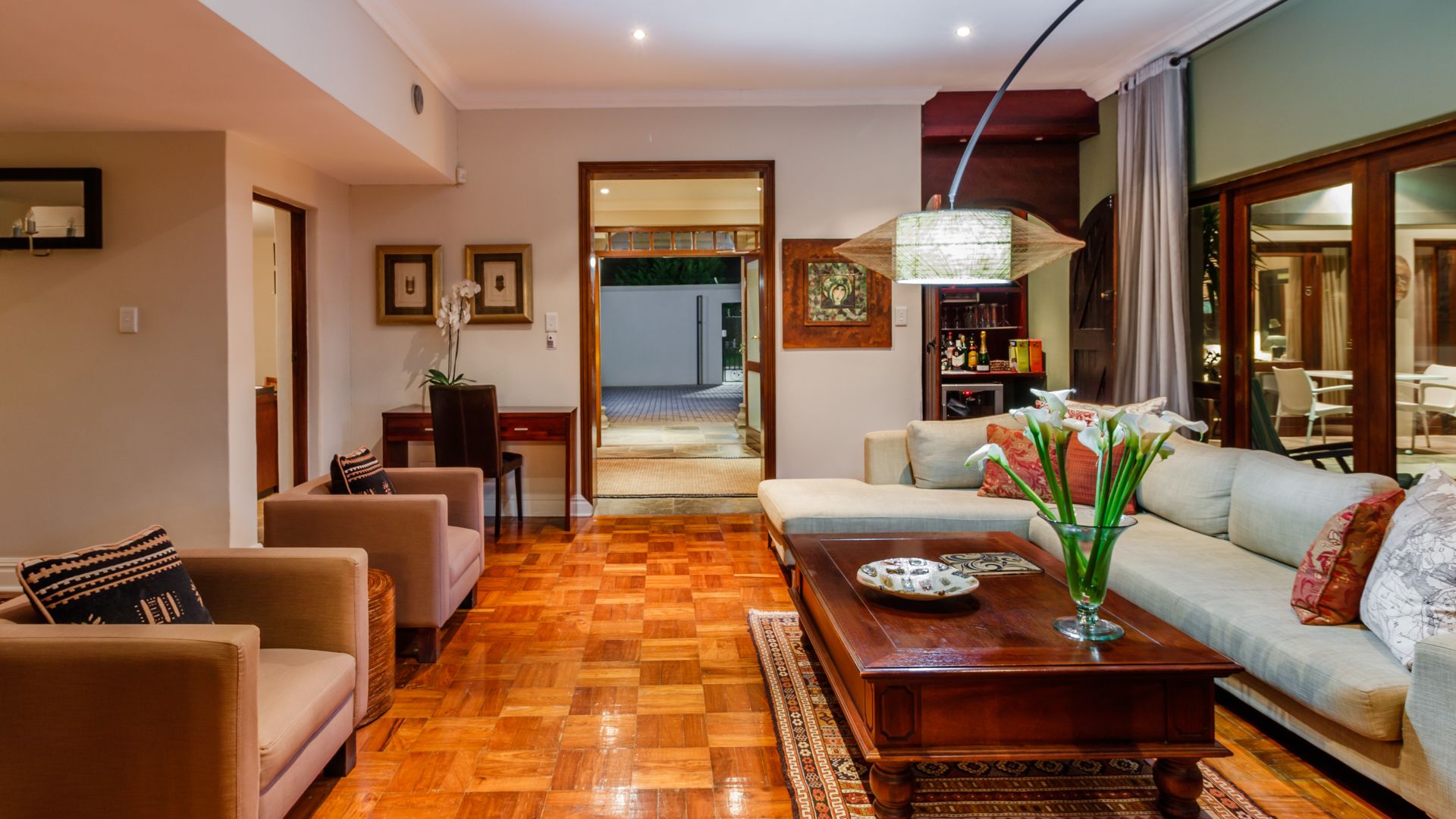 A spacious living room with a wooden parquet floor, a sofa set, a coffee table, and a dining area visible through an open doorway.