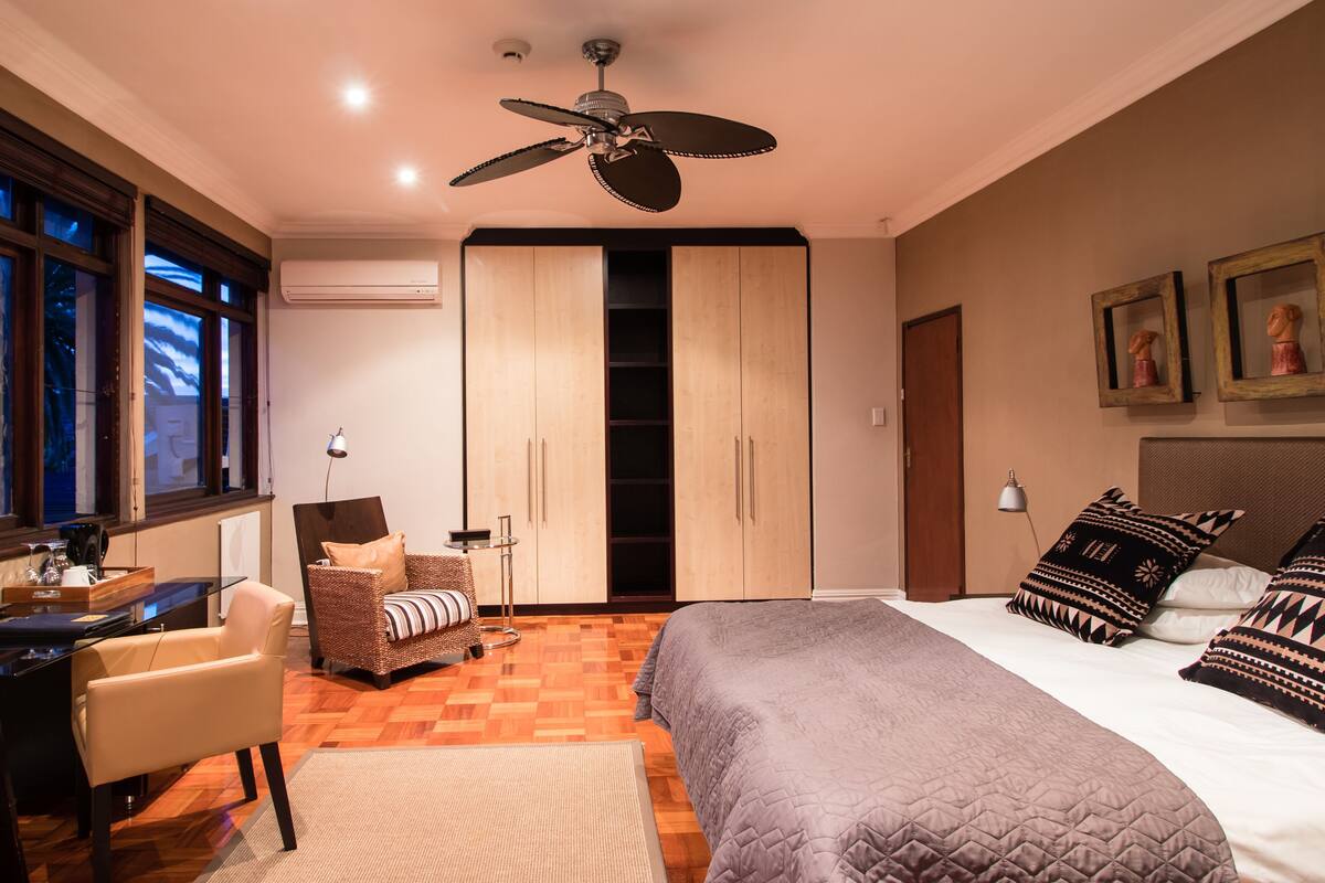 Quarto com cama, escrivaninha, cadeira, guarda-roupa e ventoinha no teto.
