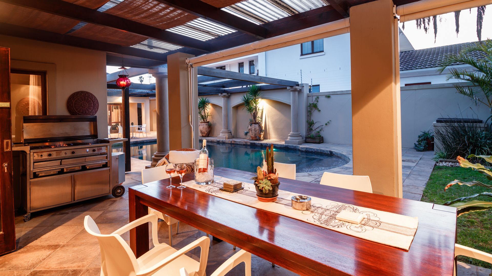 A dining area with a pool view, a grill, and potted plants.