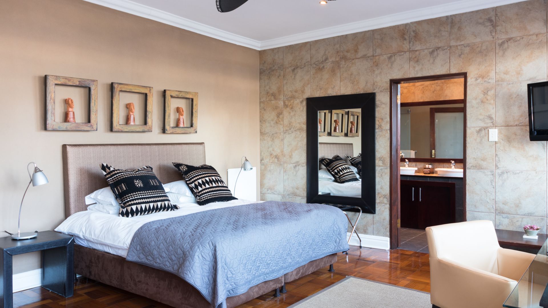 Un dormitorio moderno con una cama grande, una mesita de noche, una silla, un espejo y un baño con lavabo y espejo.